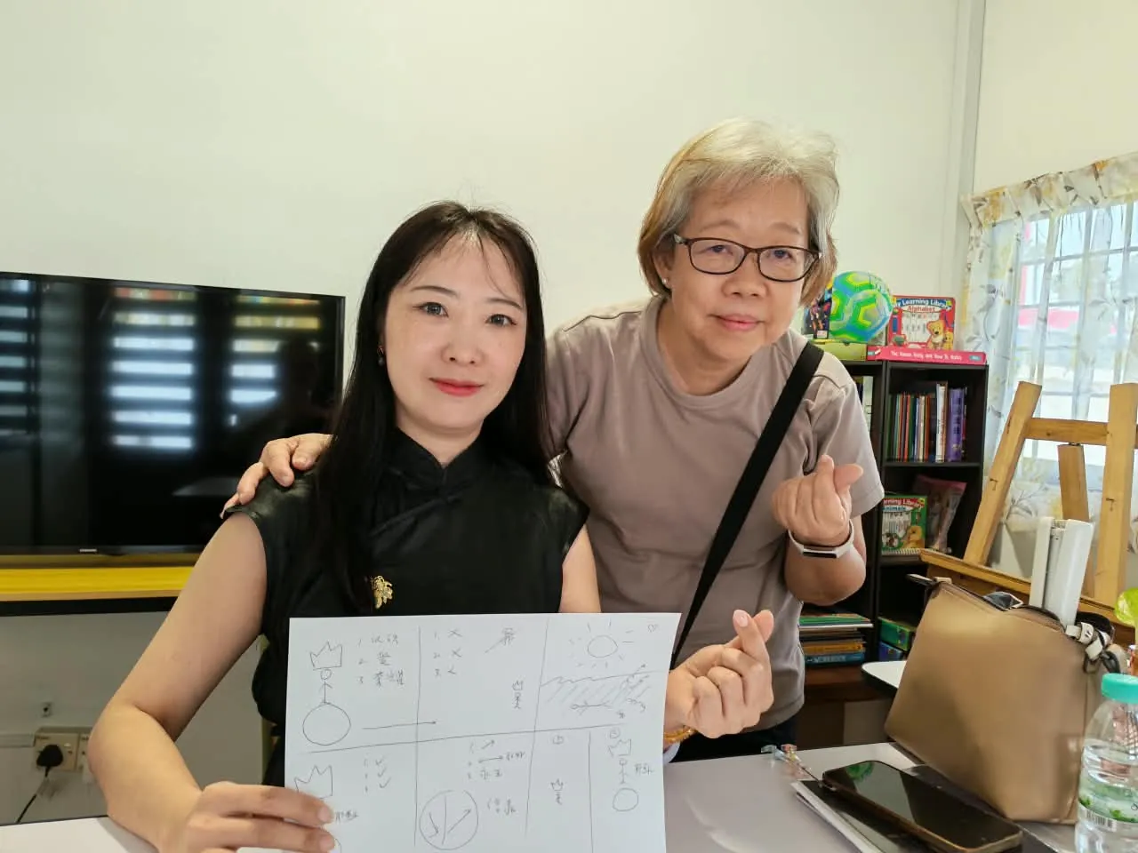 Two learners smiling, one holding up a drawing from a Zúme session