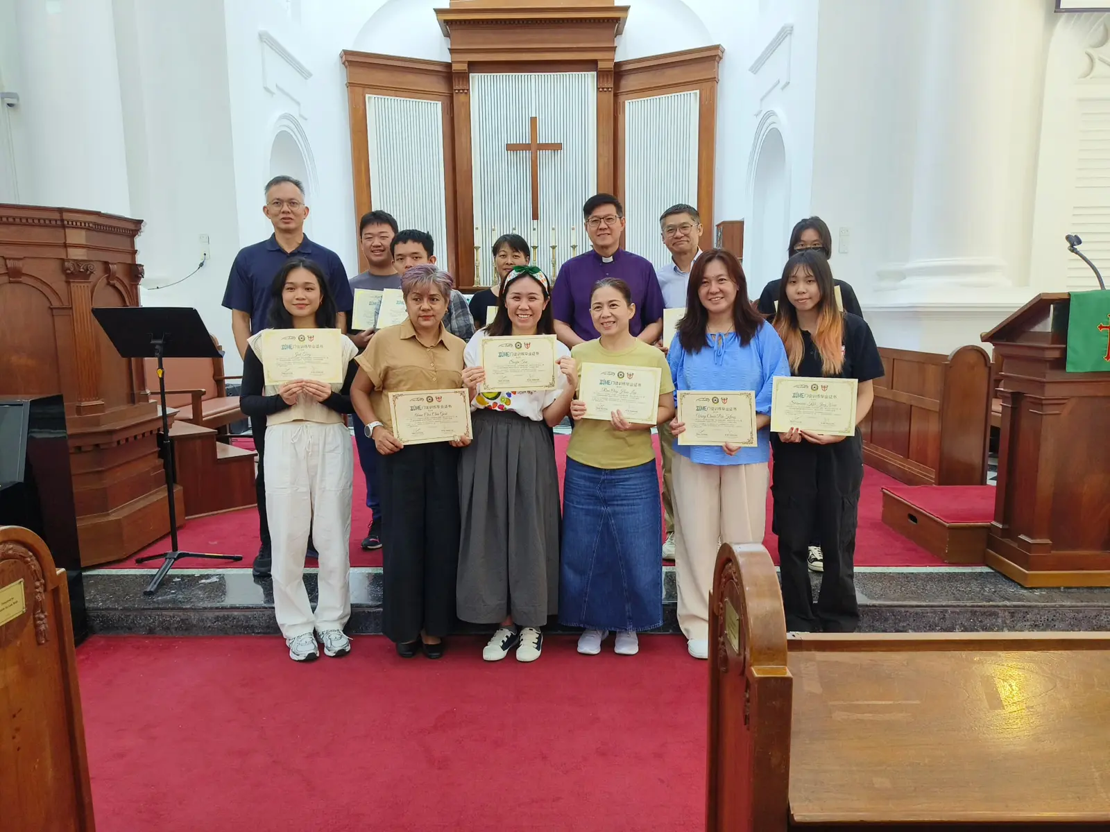 Zúme graduates holding certificates at the front of a church
