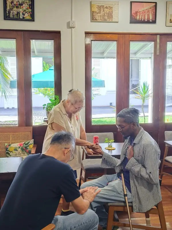 Pastor Jony kneeling to pray with an elderly man at the café